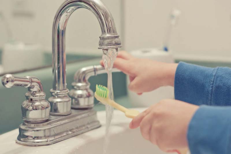 cleaning toothbrush under tap water